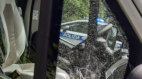 Zerbrochenes Seitenfenster eines Wohnwagens. Im Hintergrund ein italienisches Polizeiauto.